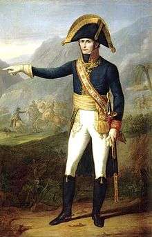 Painting of a standing man in a dark blue military uniform with white breeches and black boots. The stern-looking man, who wears a large black bicorne hat with gold edging, points to the observer's left.