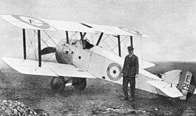 Uniformed man in peaked cap standing in front of white biplane