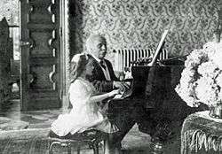 a young girl and an elderly man duetting at a grand piano