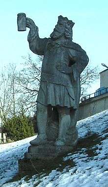 A proud statue of Gambrinus looking up at a mug of beer he holds with one hand; his other hand rests on his hip. Snow surrounds the statue.