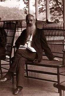 an elderly man with a long beard is seated on a veranda.