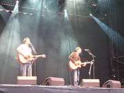 Two men playing acoustic guitar on stage in concert.