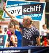 A young man waves at a parade, while a campaign sign with his name, Gary Schiff, is held up behind him.