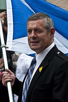 A middle-aged man wearing a suit and tie holding the Scottish flag.