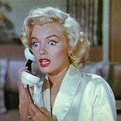 Monroe in Gentlemen Prefer Blondes. She is wearing a white dressing gown and is holding a phone. She looks shocked, with wide eyes and an open mouth.