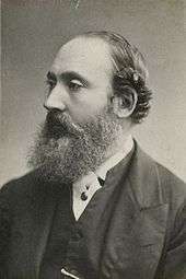 George Butler in profile, wearing a suit; his hair is receding and he has a large beard