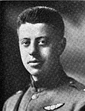 Head and shoulders of man in uniform. He has no tie; the tunic is buttoned at the neck. He wears a pair of wings on the breast and a Sam Brown belt.