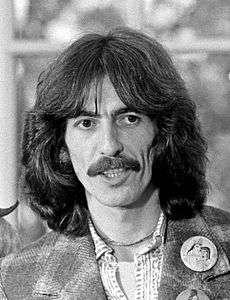 Black-and-white shot of a man in his early thirties, George Harrison, with mustache and long, dark hair.