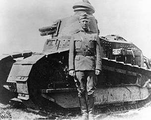 a tall, thin military officer standing in front of a world war I era tank