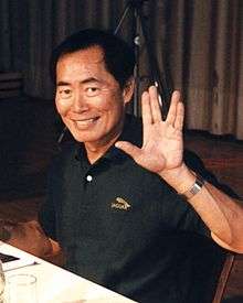 An Asian man wearing a black shirt gives a Vulcan salute.