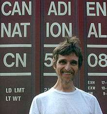 A man wearing a white t-shirt stands with the words "Canadien National" visible behind him.