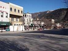 A set of attached two and three-story commercial buildings seen from across a street with a mountain behind them