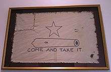 A white flag, with a five-pointed-star over the outline of a small cannon, with the words Come and Take It below.  The left corner of the flag has been torn off and sewn back on.