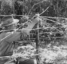 A man in a slouch hat adjusts what looks like barbed wire.