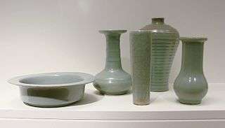 Five pieces of pale green pottery. From left to right, a cylindrical bowl with a large, flat rim, a vase with a long, thin stem and a short, almost spherical body, a tall, thin glass, a wider vase with no stem, and a small opening at the top, and a vase with a long, but wide stem and an almost spherical body.