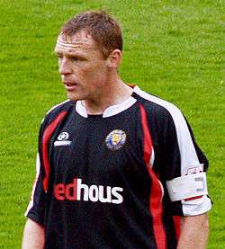 A man wearing a black, red and white football shirt during a game.