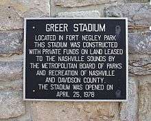 Set against a natural stone wall, a black plaque with silver text reads, "Greer Stadium. Located in Fort Negley Park this stadium was constructed with private funds on land leased to the Nashville Sounds by the Metropolitan Board of Parks and Recreation of Nashville and Davidson County. The stadium was opened on April 25, 1978.
