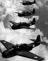 Black-and-white aerial shot of four planes (with white stars on each wing and the body) flying in formation adjacent to each other over clouds.