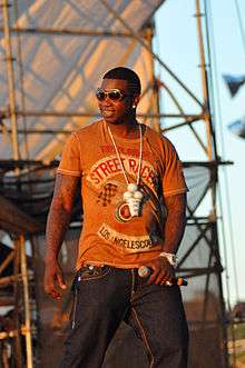 Gucci Mane performing in Williamsburg, Brooklyn on August 29, 2010. He is holding a microphone in his left hand and is wearing his signature ice cream cone medallion.