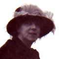 Photographic portrait of a woman wearing a hat, looking side on into camera.