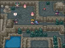 A pre-teenaged boy with black hair and a black and yellow baseball cap stands inside a dark, rocky, cave-like area. A small, blue, crocodile-like Pokémon stands behind him. Standing elsewhere in the area are two young men and one young woman, all wearing black clothes and beanies, and two small, pink, quadrupedal Pokémon.