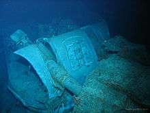 The mangled wreck of a naval gun turret. The photograph has a blue tinge, as it was taken in deep water.
