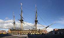 A picture of HMS Victory, the world's oldest commissioned naval ship, situated in Portsmouth's dry dock. The ship itself is missing its figurehead in this photo but retains its original sails.