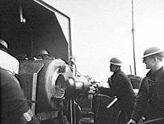 Gunners wearing steel helmets load a shell into a large calibre weapon