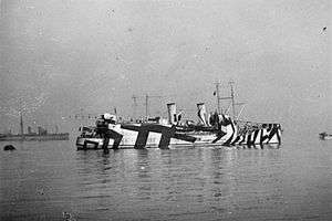 Black and white photograph of a ship with two funnels, and a crane and biplane in the stern