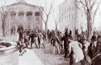 A man crumpled in a heap near a fountain in front of a building with columns. Four other men tend to the wounded man while scores of others mill about with rifles