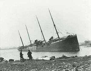 Two men observe a large beached ship with "Belgian Relief" painted on her side