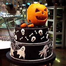 A Halloween cake decorated with ghosts, spider webs, skulls and long bones, jack-o'-lanterns and spiders. The cake is topped with a jack-o'-lantern