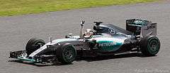 A picture of Lewis Hamilton driving a Mercedes F1 W06 Hybrid formula one car during the 2015 British Grand Prix, raising his arm in celebration after winning the race.