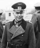 A man wearing full military uniform, including greatcoat, with an Iron Cross displayed at his neck.