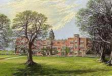 A large red-brick country manor house with trees in the foreground