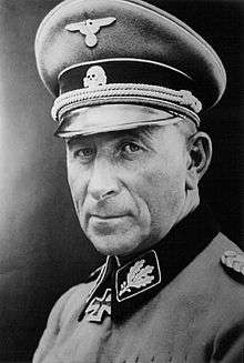 Black-and-white portrait of an older man wearing a peaked cap, military uniform with an Iron Cross displayed at his neck.