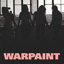 A black-and-white photograph featuring a silhouette of four women standing in a loft windowsill. Pink uppercase text at the bottom center reads "Warpaint".