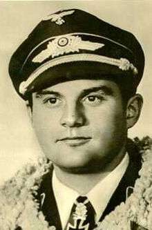 The head and shoulders of a young man, shown in semi-profile. He wears a peaked cap and a pilot's leather jacket with a fur collar, with an Iron Cross displayed at the front of his shirt collar.