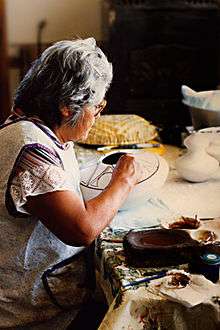 Helen Naha in her home decorating a pot in her Awatovi Star pattern