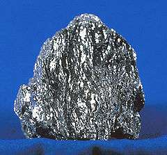A sparkling, metallic gray chunk of hematite on a blue background.