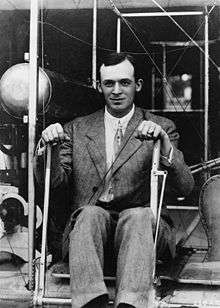 young man in business suit seated in at the controls of an early-model wright brothers airplane