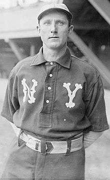 A man wearing a dark baseball uniform with ornate "N" and "Y" over each breast and a white baseball cap