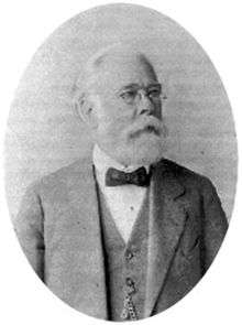 Older, bearded man in suit, spectacles and bow tie