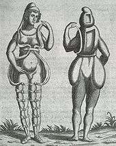A front and back illustration of a Renaissance-era hermaphrodite showing a person with female facial features, breasts, and what appears to be a small penis or large clitoris. She wears a small hood and open robe tied multiple times around the legs. Where it opens in the front, the apparent rear appearance shows it to be perhaps a shell of some kind, as one with her body Two squares are missing from her the back of her head and torso. She has no buttocks.