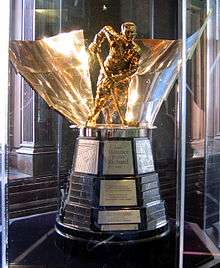 A trophy featuring a brass-coloured statuette of Richard atop a wood base with metal plates bearing the inscription of the trophy's winners