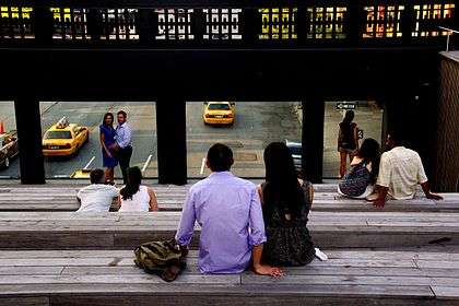 People sitting on wooden benches in a small amphitheater, which is elevated over a city street