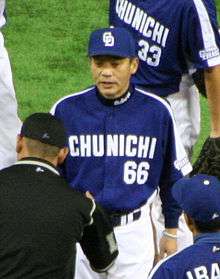 Japanese man wearing a blue and white uniform greets an umpire