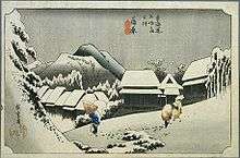  A village in a mountainous landscape. A man with a conical hat and a cane, and a saddled horse can be seen in the foreground. Japanese characters are seen in the down left and top central parts of the image.