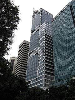 Ground-level view of a 40-storey building with a glass facade and rectangular cross section; three levels of windows recede inward at various points up the tower, and a spire is present on the roof.