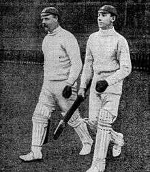 Two cricketers coming out of a pavilion, ready to bat
